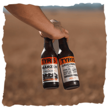 una mano sostiene dos botellas de cervezas artesanas Tyris al aire libre, una es la versión original y la otra sin gluten ideal para celiacos