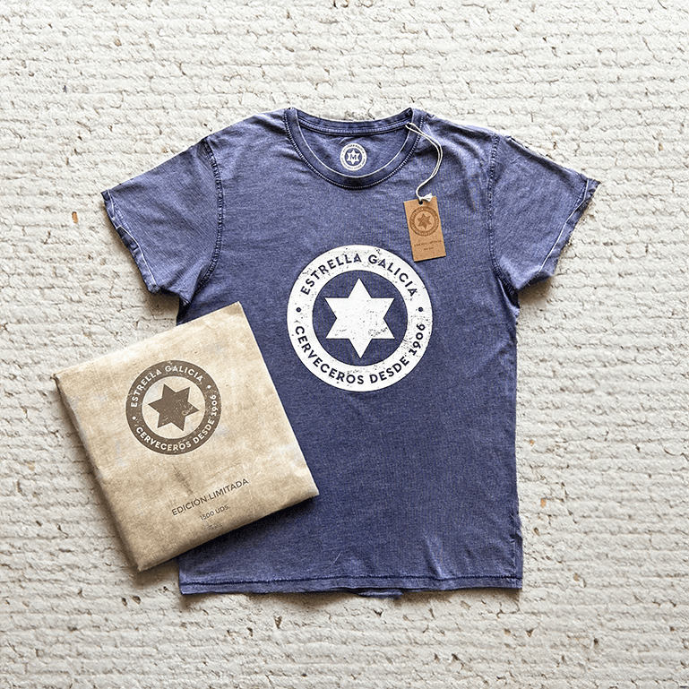 Camiseta azul de Estrella Galicia con el logo Cerveceros desde 1906 y un sobre marrón