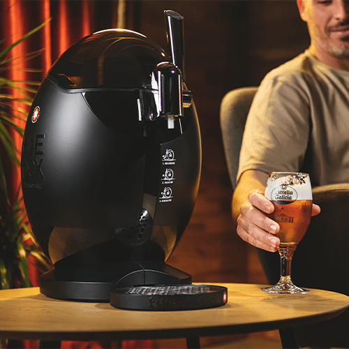 Hombre sostiene una copa de cerveza Estrella Galicia al lado de un Huebox