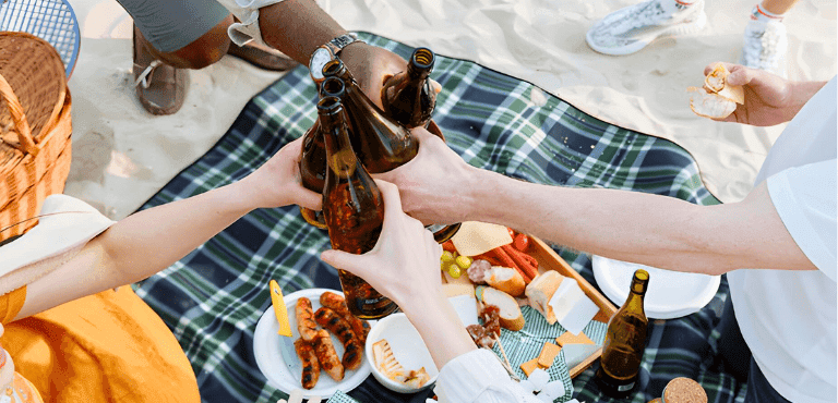 personas se reúnen en una playa con aperitivos y cerveza