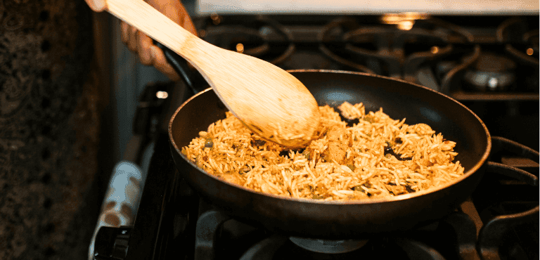 una cuchara de madera mueve un arroz en una sartén