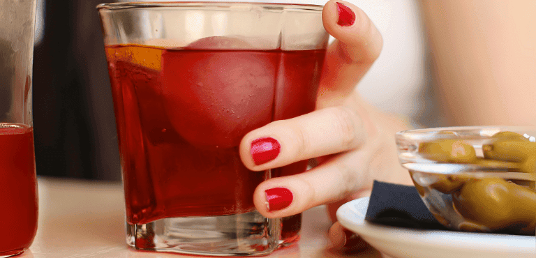 una mano sostiene un vaso de vermut rojo