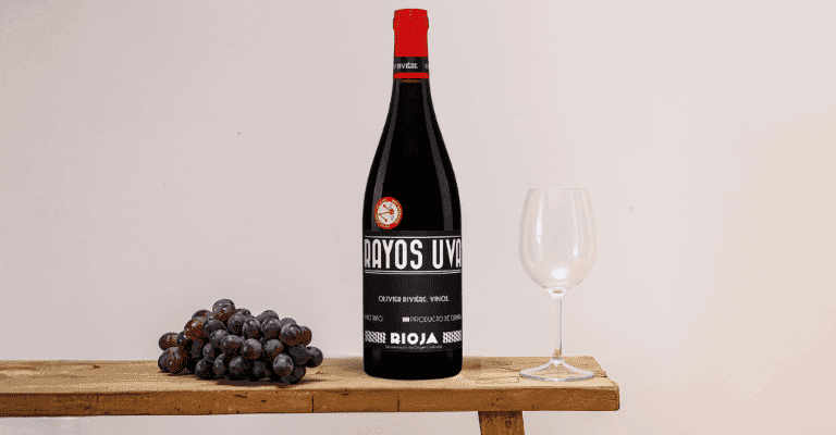 Una botella de vino Bodegas Olivier Riviere y una copa sobre una mesa con uvas