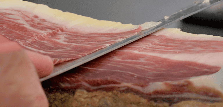 una pieza de jamón cortada a mano con un cuchillo filoso