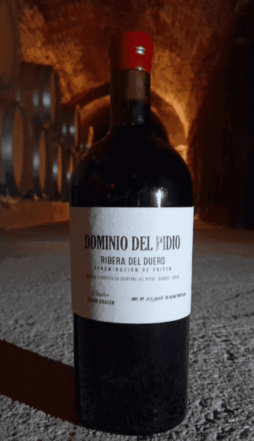 una botella de vino Dominio del Pidio con unos barriles de fondo