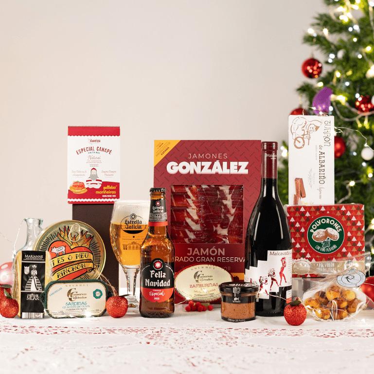 lote de Navidad con vino, cervezas, dulces, conservas, queso y más. sobre una mesa con un árbol de navidad de fondo