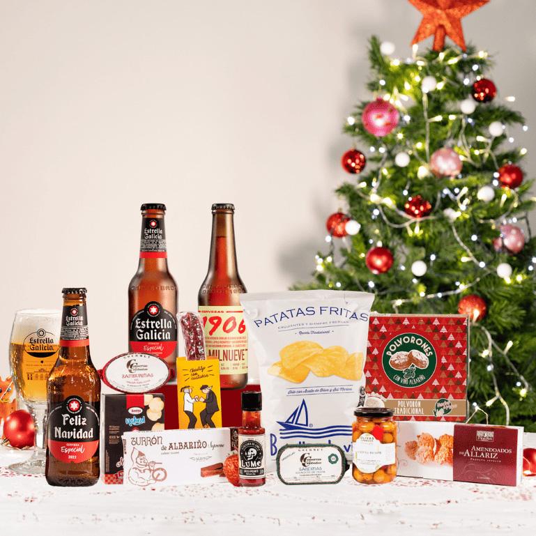 lote de Navidad con vino, cervezas, dulces, conservas, queso y más. sobre una mesa con un árbol de navidad de fondo