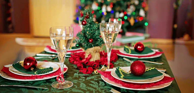 mesa navideña con platos y copas y un árbol de Navidad de fondo