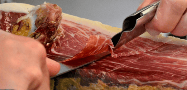 Una pieza de jamón ibérico de bellota siendo loncheada para disfrutar en verano a una temperatura adecuada.