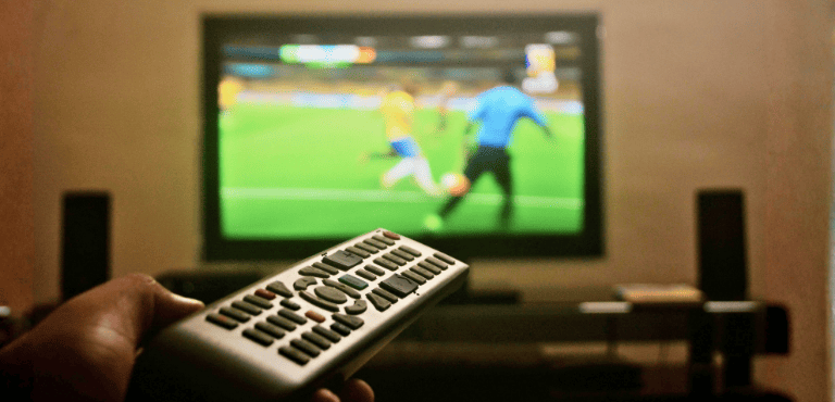 Una persona sostiene un control remoto mientras observa un partido de fútbol sin perder las mejores jugadas.