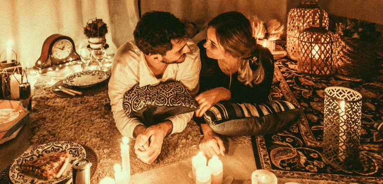 Un pareja enamorada celebra San Valentín en casa con una cena romántica, cervezas, velas y comida