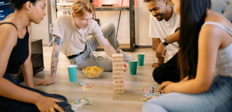 Un grupo de amigos juega juegos de mesa, mientras beben cervezas y se divierten en casa con planes caseros baratos ideales para días fríos o para cualquier temporada del año
