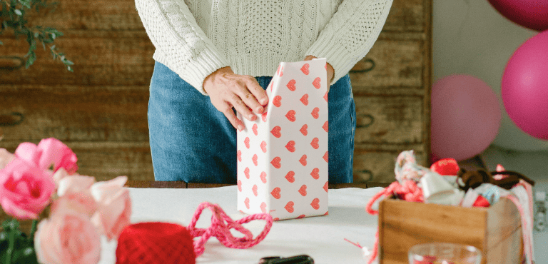 Una persona envuelve una caja de regalo cervecero con una envoltura de corazones para sorprender en San Valentín