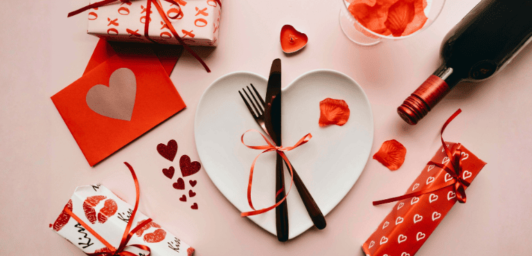 un plato en forma de corazón, unas cartas, botella de vino y cajas de regalos perfectos para San Valentín para disfrutar en pareja con opciones originales que sorprenden