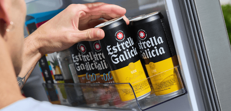 Un hombre agarra una lata de cerveza sin gluten de Estrella Galicia de su nevera, al lado hay lata de otras cervezas de Estrella Galicia sin gluten y sin alcohol, que son opciones ideales para celiacos y personas que quieren cuidar su salud