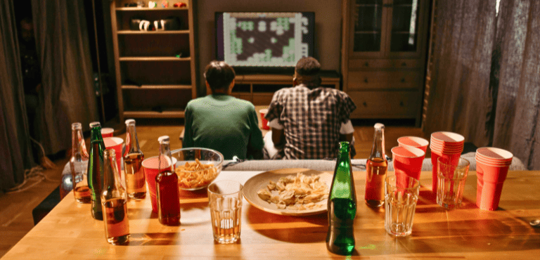Dos jovenes ven películas y juegan mientras comparten el aperitivo perfecto para tardes de peli y manta con cerveza, snacks y mucho más