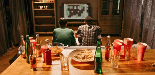 Dos jovenes ven películas y juegan mientras comparten el aperitivo perfecto para tardes de peli y manta con cerveza, snacks y mucho más