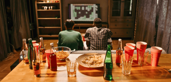 Dos jovenes ven películas y juegan mientras comparten el aperitivo perfecto para tardes de peli y manta con cerveza, snacks y mucho más