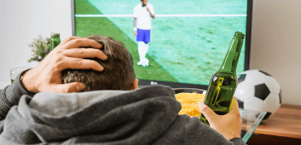 Un hombre ve la gran final de fútbol por todo lo alto con un picoteo gourmet perfecto para disfrutarla y compartir con amigos.