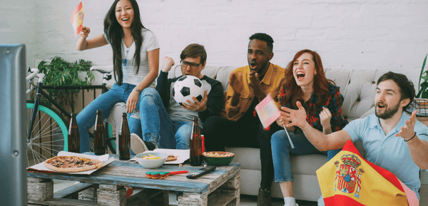 Grupo de jóvenes se reúne para ver un partido de fútbol en televisión mientras comen platos preparados fácilmente durante la prórroga.