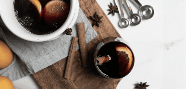 Un cazo con vino caliente humeante lleno de aromas especiados, acompañada de un vaso de vino caliente que emana un perfume reconfortante y burbujeante