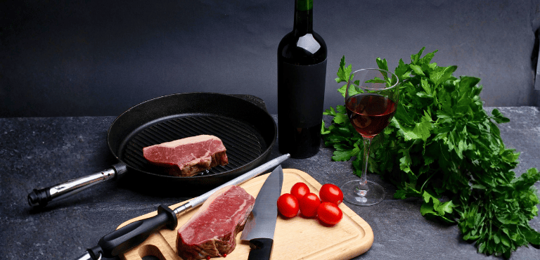 Un pedazo de carne de ternera con una botella de vino tinto y una copa, para preparar una de las recetas con vino tinto que tienen un sabor intenso y delicioso y son fáciles de hacer