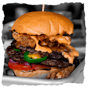 una jugosa hamburguesa de carne de res con pan, salsas A Factoría do Lume, queso cheddar fundido y crujientes pepinillos sobre un fondo rústico y ligeramente quemado por la parrilla en la carne 