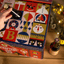Una persona saca una botella de Rivera Reposada del Calendario de Adviento de cervezas Bigcrafters en caja con forma de casita navideña ilustrada por Yarza Twins.