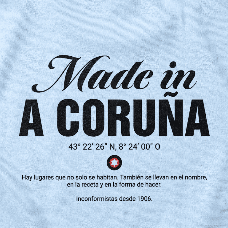 Primer plano de tela de algodón azul claro de camiseta con serigrafía negra detallada del texto "Hecho en A Coruña", coordenadas, logotipo de estrella y una cita en español.