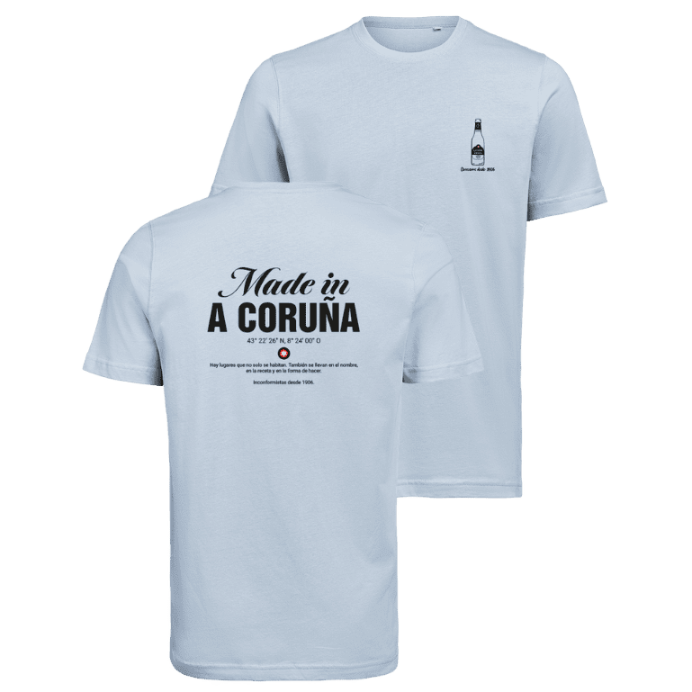 Camiseta Estrella Galicia de tela de algodón azul claro de camiseta con serigrafía negra detallada del texto "Hecho en A Coruña", coordenadas, logotipo de estrella y una cita en español.
