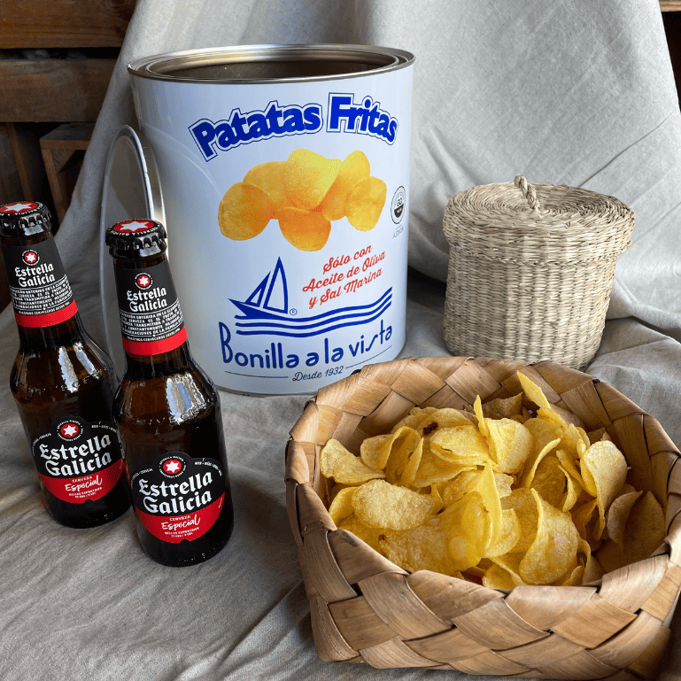 Varias botellas de cerveza Estrella Galicia Especial de 25 cl, donde la suavidad del lúpulo y la riqueza del malta se combinan armoniosamente con el crujiente y salado sabor de una lata de patatas Bonilla a la vista de 500 g