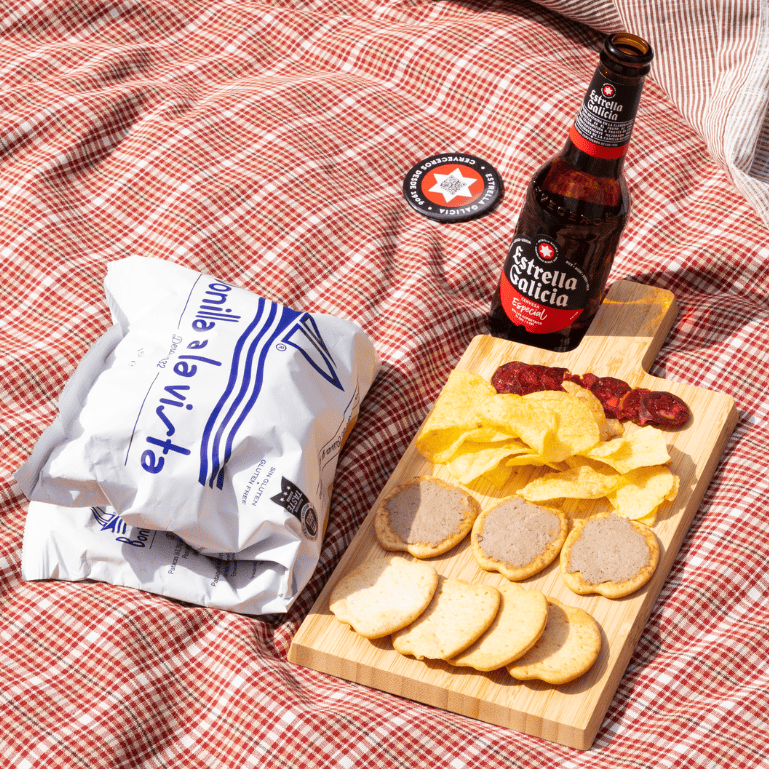 Un pack de Estrella Galicia Especial con patatas Bonilla A La Vista en un picnic al aire libre con embutidos y galletas, un aperitivo que resulta refrescante y delicioso para picotear porque ambos productos combinan bien