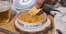 un paté de bacalao de La Curiosa, una fusión sorprendente de bacalao islandés con salsa de aceite, cebolla y tomate, acentuada por dulces compotas de manzana confitada, que equilibra sabores salados y dulces en un paté exquisito
