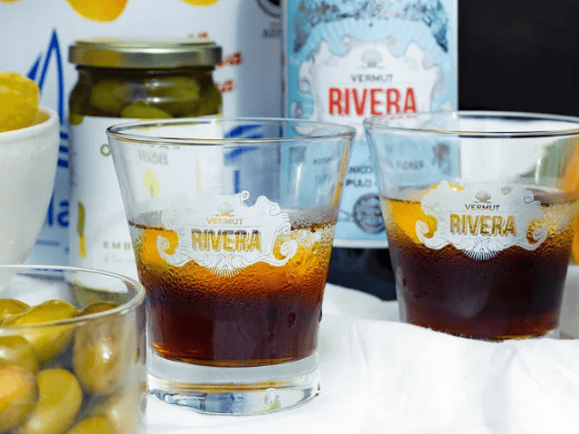 dos vasos y una botella de Vermut Rivera rojo, clásico con lúpulo cascade y pétalos de rosa, aromático y lupulado, acompañado por olivas verdes para un aperitivo premium