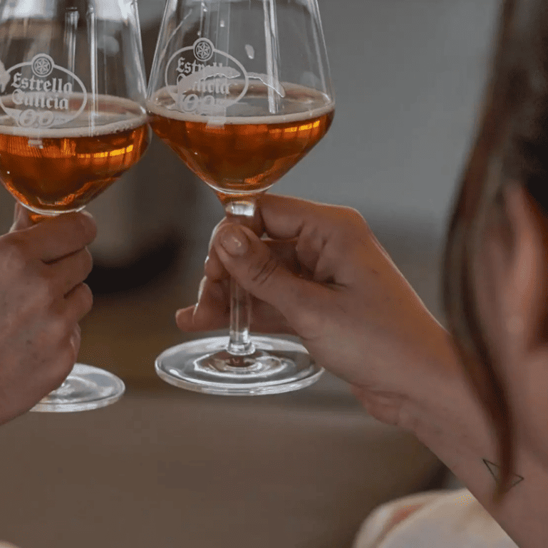 Dos personas brindan con copas de Estrella Galicia 0,0 mientras disfrutan de un masaje relajante, combinando celebración y tranquilidad.