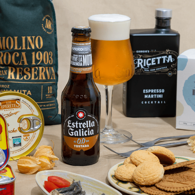 Una mesa llena de cerveza Estrella Galicia con copa, cocteles, galletas, conservas y aperitivos que combinan bien para un picoteo.