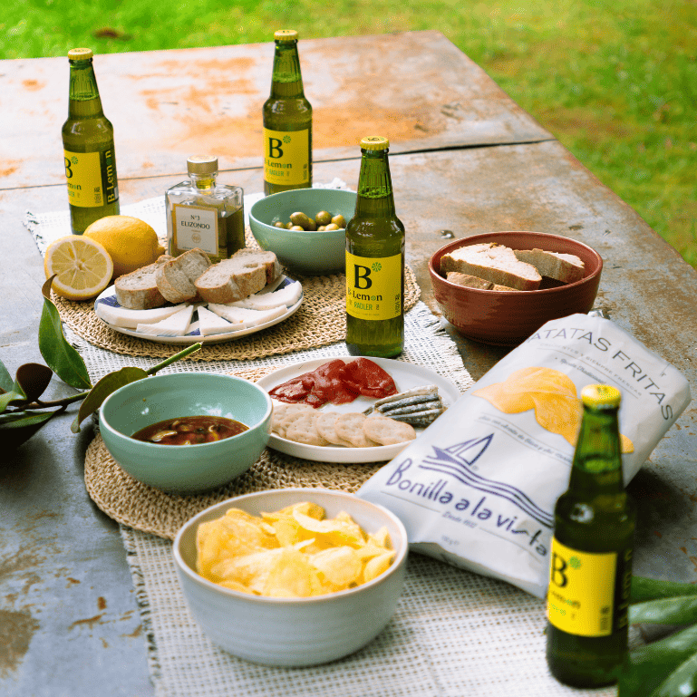 Cervezas B-Lemon Radler con patatas fritas Bonilla a la Vista, embutidos, pan y olivas para un picnic al aire libre sabroso y refrescante.
