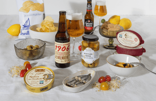 un pack de regalo con cervezas Estrella Galicia y 1906, aceitunas, consevas, gallegas, patatas fritas y más aperitivos para una experiencia gourmet completa.