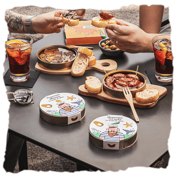 Una tabla con pan y latas de conservas de carne marca A Casa Da Avoa, hecha de forma tradicional con la receta de la abuela, perfectas para un picoteo al aire libre.