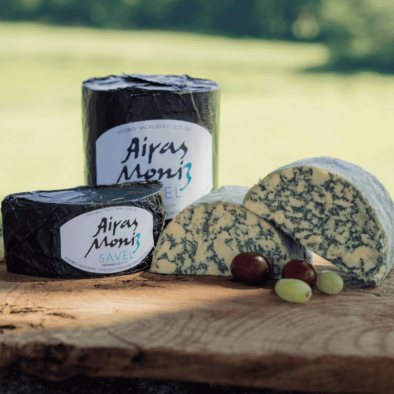 Quesos Savel de Airas Moniz al aire libre con uvas, un queso azul único y rebelde, elaborado con leche cruda de vaca Jersey, que sorprende por la intensidad de sus vetas azul-verdosas y una textura tan untuosa que se funde en la boca como mantequilla.