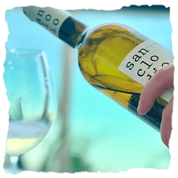 una persona sirve una copa de vino Sanclodio, un vino blanco color amarillo oro con reflejos limón, aromático y fresco, revelando la esencia de los viñedos graníticos de Leiro